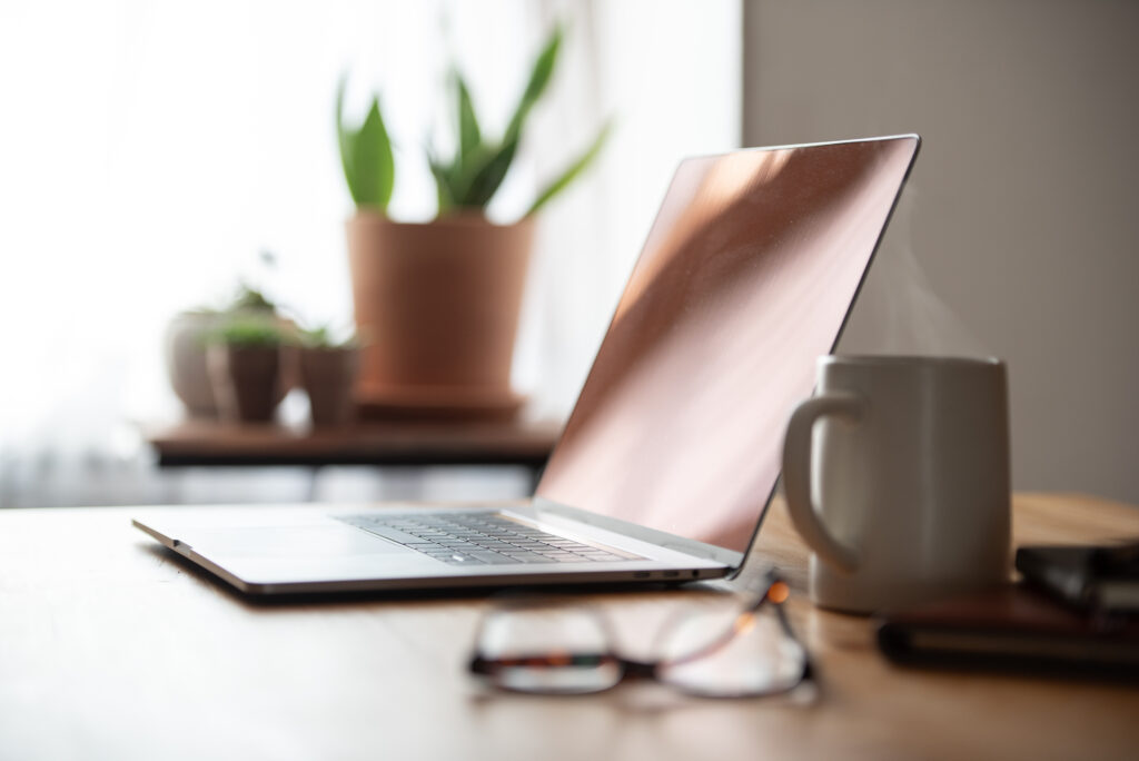 Shallow depth of field side view of a home office with a laptop, steaming coffee, and eyeglasses.