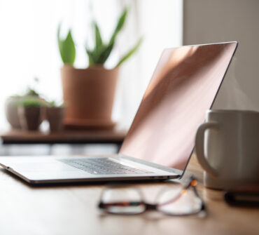 Shallow depth of field side view of a home office with a laptop, steaming coffee, and eyeglasses.